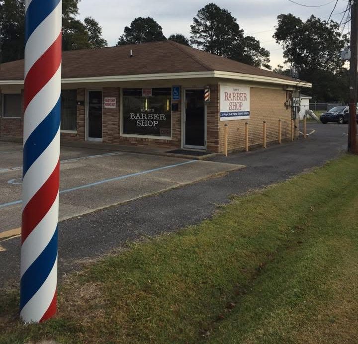 The storefront of Terry's Barber Shop with its large red, white, and blue barber pole out front